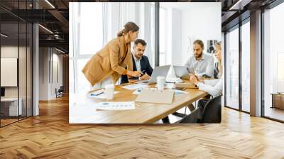 Group of a young office employees dressed casually in the suits having some office work at the meeting table in the bright office Wall mural