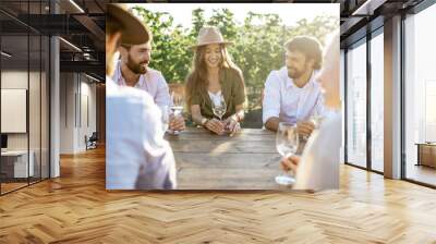 Group of a young people drinking wine and having fun together while sitting at the dining table outdoors on the vineyard on a sunny evening Wall mural