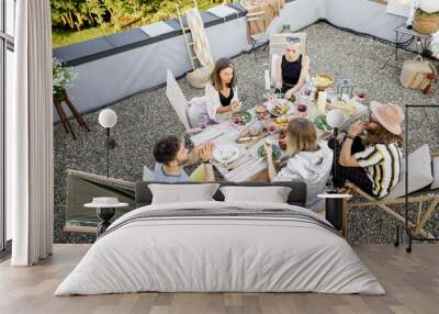 Group of friends have a festive dinner, sitting at beautifully decorated wooden table full of healthy food on a roof terrace. View from above Wall mural