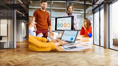 group of young coworkers dressed casually working together on the computers with some charts sitting Wall mural