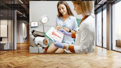 Gynecologist showing a picture with uterus to a young woman patient, explaining the features of women's health during a medical consultation in the office Wall mural