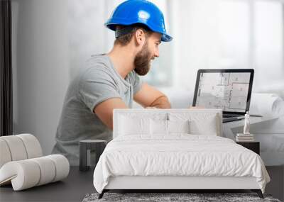 Handsome architect or foreman in helmet working with laptop on the apartment drawings at the structure white interior Wall mural