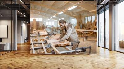 Handsome carpenter in uniform gluing wooden bars with hand pressures at the carpentry manufacturing Wall mural