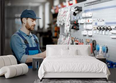 Handsome electrician in workwear choosing electrical goods standing with smart phone in the building shop Wall mural