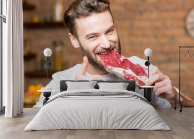 Handsome man biting raw meat on the kitchen Wall mural