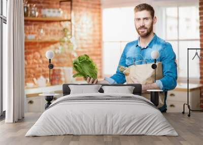 Handsome man in blue shirt unpacking healthy food from the shopping bag on the kitchen Wall mural