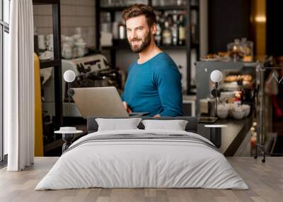 Handsome man in blue sweater working with laptop at the bar of the modern cafe interior Wall mural