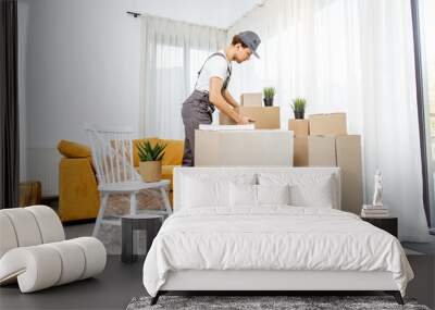 Handsome mover in workwear performing professional delivery of a goods and furniture during relocation process to a new house, interior view Wall mural