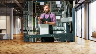 Handsome packer in working apron with box on the packaging line at the manufacture. Wall mural