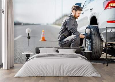 handsome road assistance worker in uniform changing car wheel on the highway Wall mural