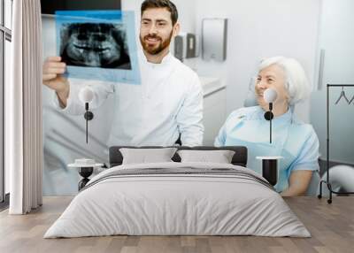 Happy elder woman during the consultation with handsome dentist showing panoramic x-ray in the dental office Wall mural