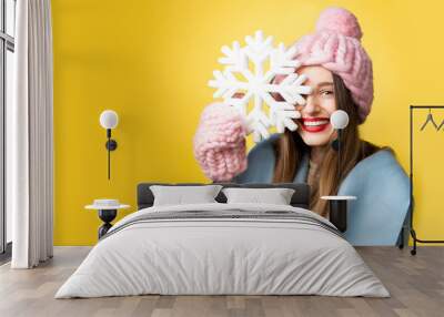 Happy woman in colorful winter clothes holding a beautiful snowflake standing on the yellow background. Happy winter concept Wall mural