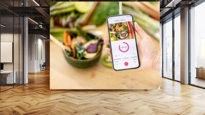 Holding smart phone with running mobile application for track calories consumed on background of healthy food ingredients. Concept of modern technology in proper nutrition Wall mural