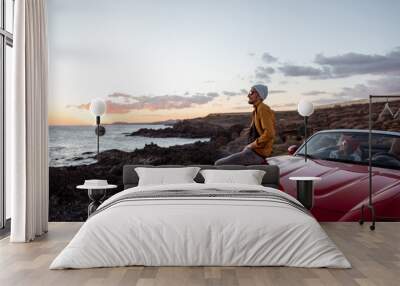 Lifestyle portrait of a man on the rocky coast during a sunset, traveling with woman by car Wall mural