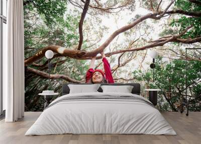 Lifestyle portrait of a woman dressed casually in red clothes enjoying while traveling in the rainforest, hanging on the tree branch Wall mural