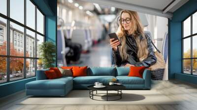 Lifestyle portrait of a young businesswoman sitting with smart phone at the modern train Wall mural