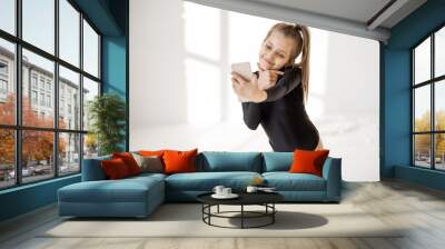 Little girl making selfie on phone or record video to social networks during a sports break at gymnastics class. Involvement in gadgets of generation z concept Wall mural