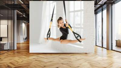 Little girl stretching on suspension straps, doing twine while practicing gymnastics at gym Wall mural