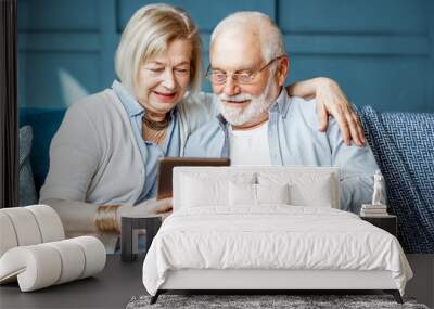 Lovely senior couple dressed casually using digital tablet while sitting together on the comfortable couch at home Wall mural