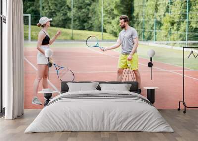 Male instructor teaching young woman to play tennis on the tennis court outdoors Wall mural