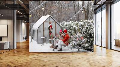 Man and woman have romantic dinner, while sitting together by the table at beautifully decorated snowy backyard. Young family celebrating winter holidays Wall mural