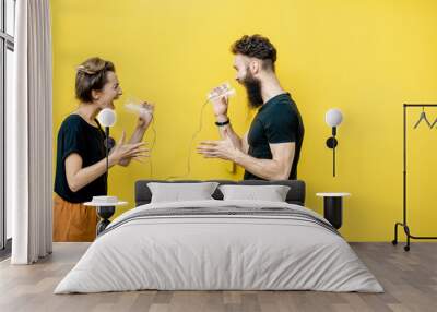 Man and woman talking with string phone, shouting on each other on the yellow background. Concept of communication and misunderstanding Wall mural