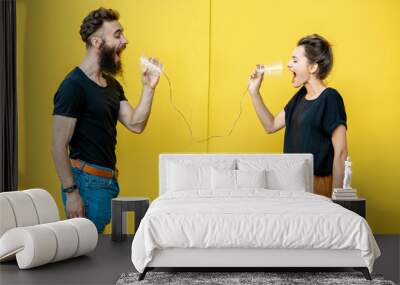 man and woman talking with string phone, shouting on each other on the yellow background. concept of Wall mural