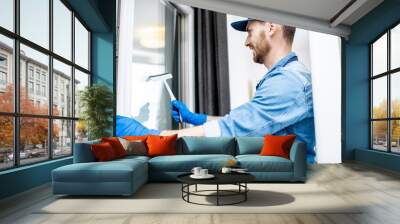 Man as a professional cleaner in blue uniform washing window with rubber brush indoors Wall mural