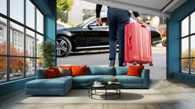 Man carries red suitcase to a car, cropped view from below. Concept of chauffeur service and business trips Wall mural