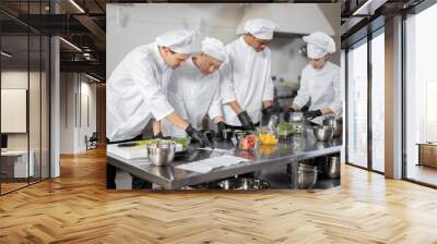 Multiracial team of cooks mixing ingredients for take away food in professional kitchen. Concept of dark kitchen for cooking for delivery. Idea of teamwork in a restaurant. Diverse people at job Wall mural