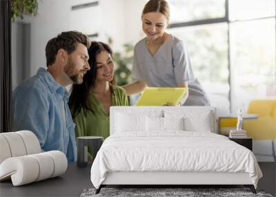 Nurse communicates with a man and woman, showing some paper before a doctors appointment in waiting room of a modern clinic. Medical service, support and care concept Wall mural