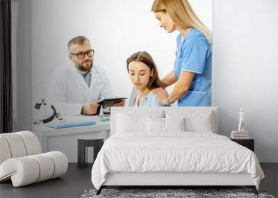 Nurse supporting young patient feeling sad during a medical consultation with senior doctor in the white office Wall mural