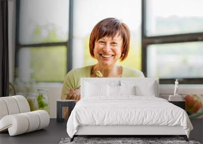 Portrait of a beautiful older woman with green healthy food on the table indoors on the window background Wall mural