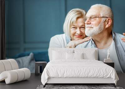 Portrait of a beautiful senior couple embracing each other, sitting on the couch at home Wall mural