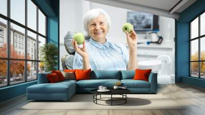 Portrait of a beautiful senior woman with healthy smile holding green apples at the dental office Wall mural