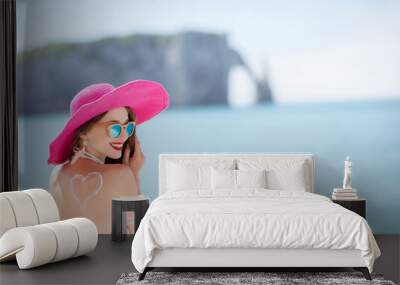 Portrait of a beautiful smiling woman in pink hat with sunscreen heart shape on her shoulder having a sunbath on the beach Wall mural