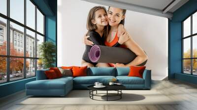 Portrait of a cheerful sports mom and little daughter sitting together with yoga mats during sports activities indoors. Close relationships with mother and sports in childhood Wall mural