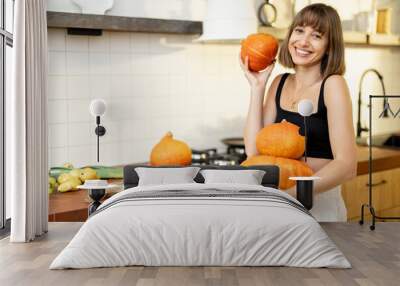 Portrait of a cheerful woman holds pumpkins while cooking healthy food in kitchen. Concept of vegetarian food and autumn pumpkin menu Wall mural