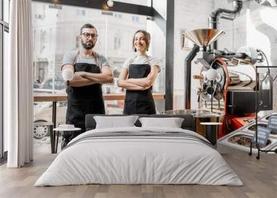 Portrait of a couple of baristas in uniform standing together in the coffee shop with coffee roasting machine on the background Wall mural