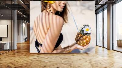 Portrait of a cute summer girl with exotic fruit shaded with palm leaves on the sandy beach Wall mural