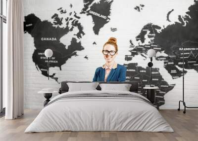 Portrait of a female travel agent dressed in the suit standing indoors on the world map background Wall mural