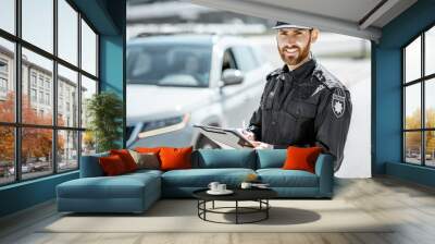 Portrait of a handsome policeman in uniform standing in front of a car on the roadside Wall mural