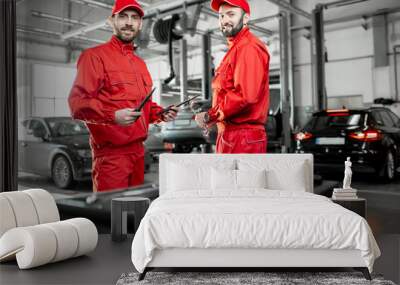 Portrait of a two handsome auto mechanics in red uniform standing with working tools at the car service Wall mural