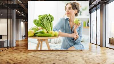 Portrait of a young and beautiful woman sitting with healthy green and fresh food indoors in the bright living room with green plants at home Wall mural