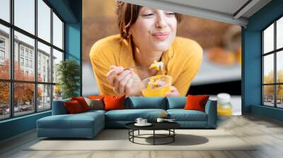 Portrait of a young and cheerful woman eating chia pudding, having a snack or breakfast in the kitchen. Concept of dieting, healthy eating and wellness Wall mural