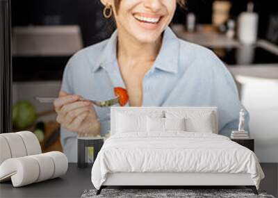 Portrait of a young and cheerful woman eating healthy salad on the kitchen at home. Healthy eating, food and lifestyle concept Wall mural