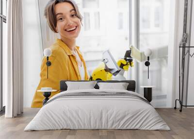 Portrait of a young and cheerful woman washing windows with a special cleansing device at home. Concept of a professional housekeeping Wall mural