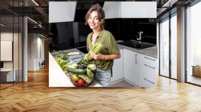 Portrait of a young and cheerful woman with healthy raw food on the kitchen at home. Vegetarianism, wellbeing and healthy lifestyle concept Wall mural