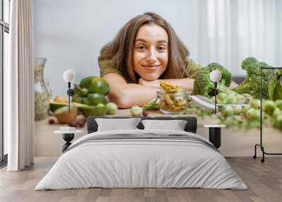 Portrait of a young cheerful woman with lots of healthy green food on the table. Concept of vegetarianism and well-being Wall mural