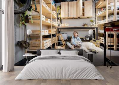 Portrait of a young handywoman sitting with her huge white dog in the home workshop. DIY concept Wall mural